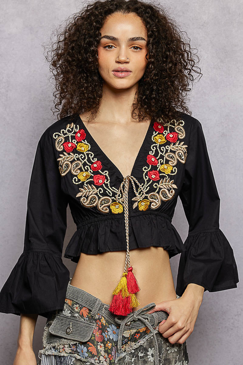 Black cropped blouse with V-neck, floral embroidery at bust, and gathered peplum hem