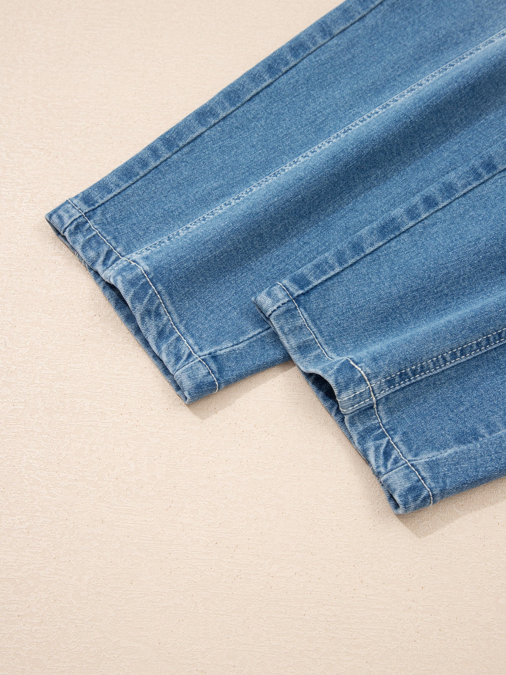 Hem cuff detail on washed medium-wash barrel jeans with visible stitching