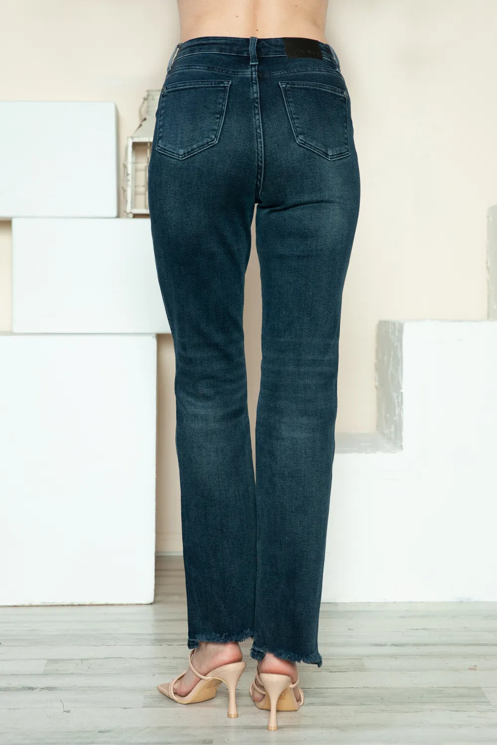 Back view of dark blue straight jeans with patch pockets and raw hem