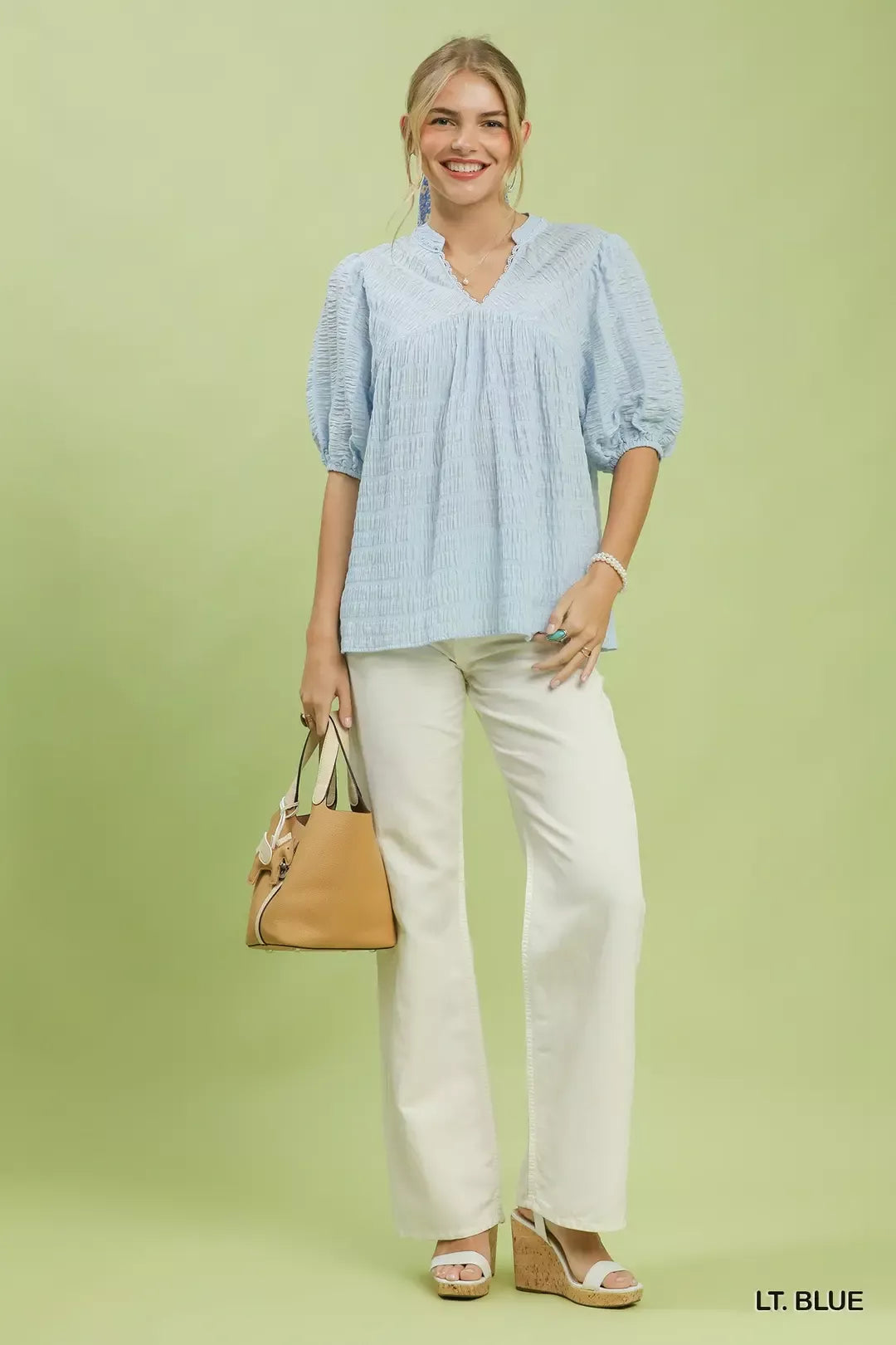 Light blue textured puff-sleeve blouse with V-neck worn with white pants