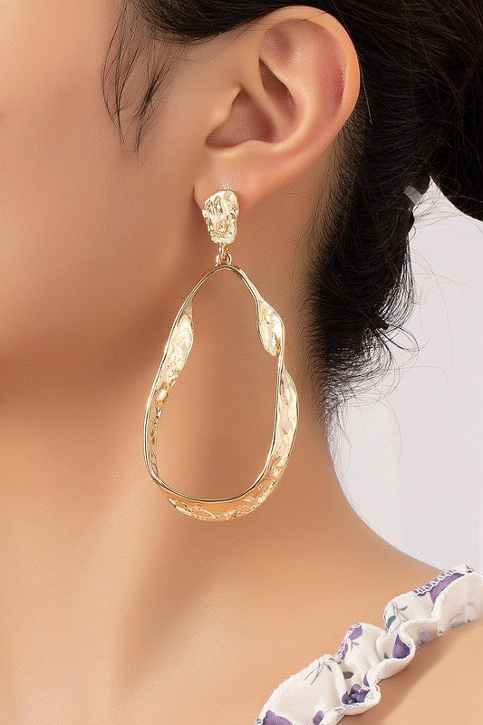 Close-up: gold hammered twisted metal hoop earring with teardrop oval shape