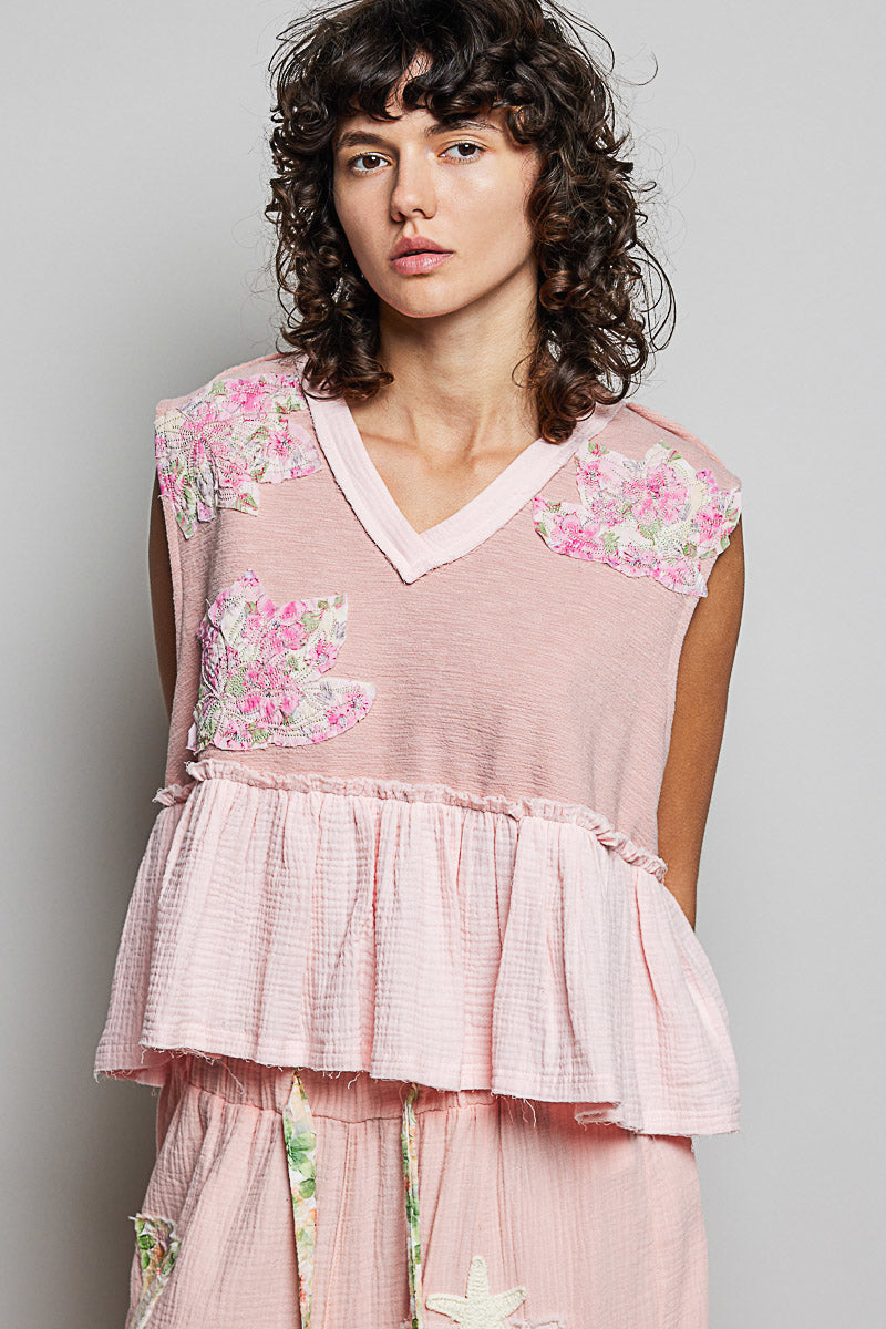 Powder pink V-neck sleeveless top with floral patch accents and layered ruffle hem