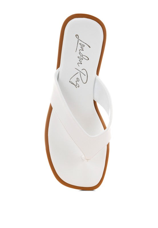 White thong flats with toe-post strap and tan outsole, textured sole underside view
