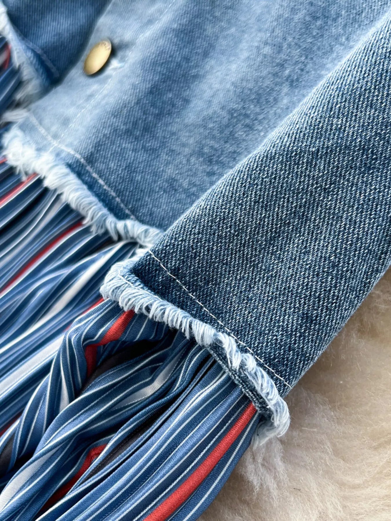 Detalle del bajo: denim azul con borde deshilachado y franja inferior a rayas multicolor