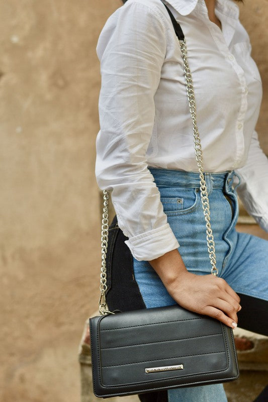 Dora crossbody bag con solapa y cierre; acabado negro liso y correa de cadena