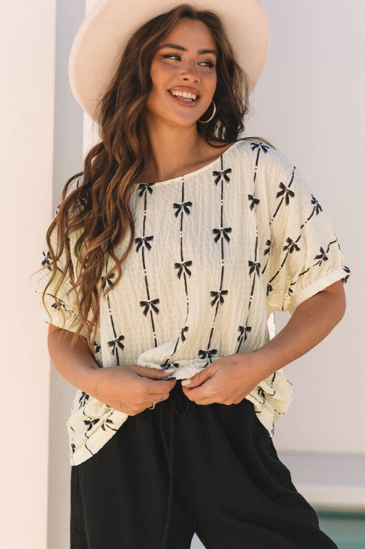 Bow-texture short puff sleeve top in cream with black bow-and-line pattern and rounded neckline
