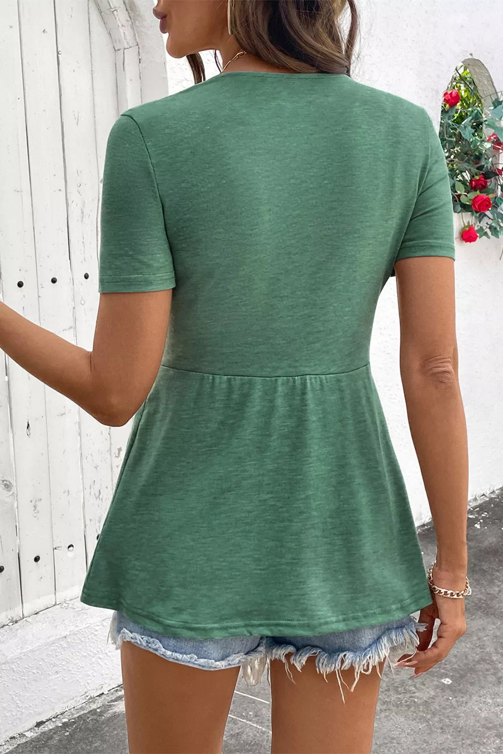 Back view of green short-sleeve V-neck blouse with gathered peplum hem