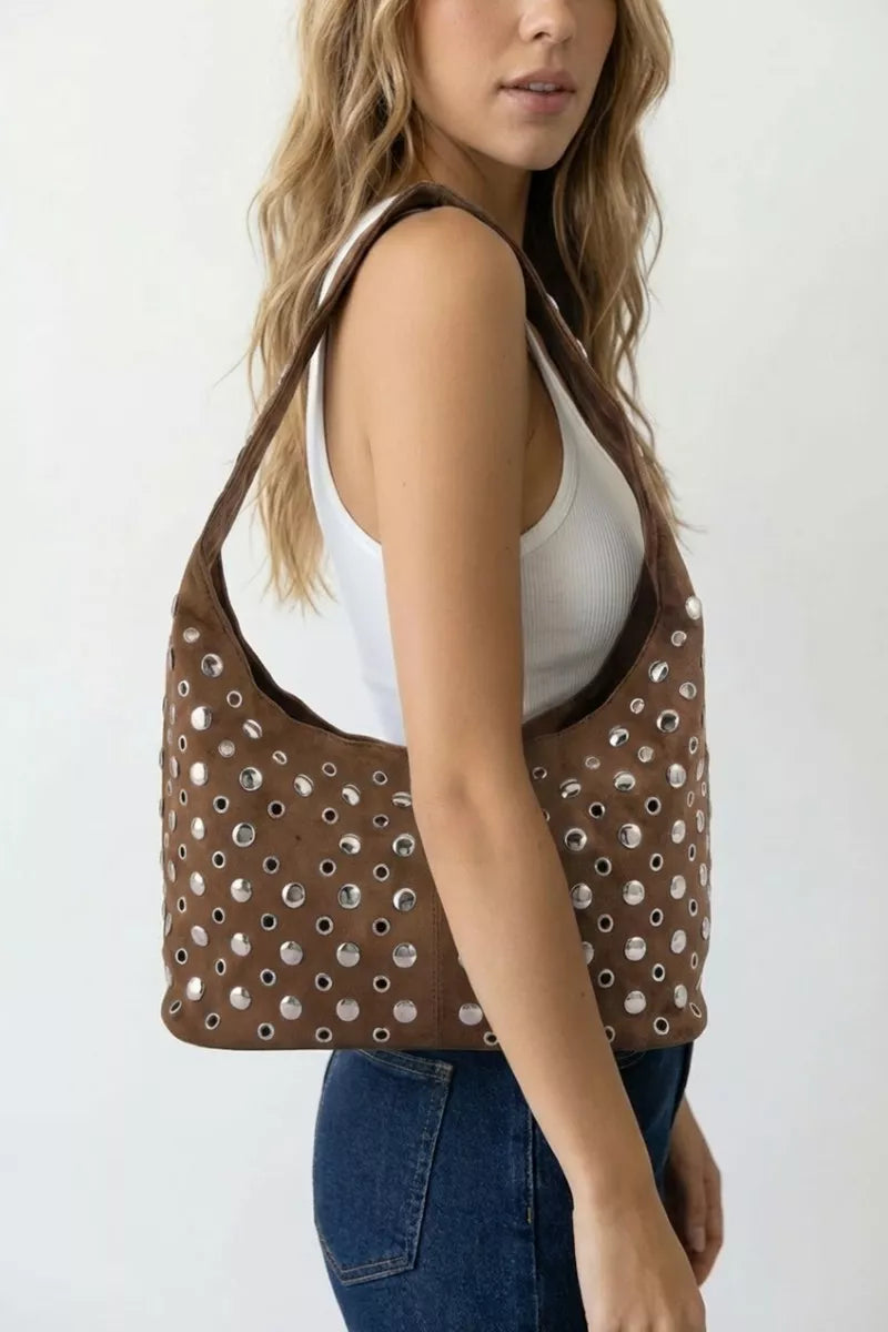 Model holding a brown rivet-studded shoulder bag over denim jeans