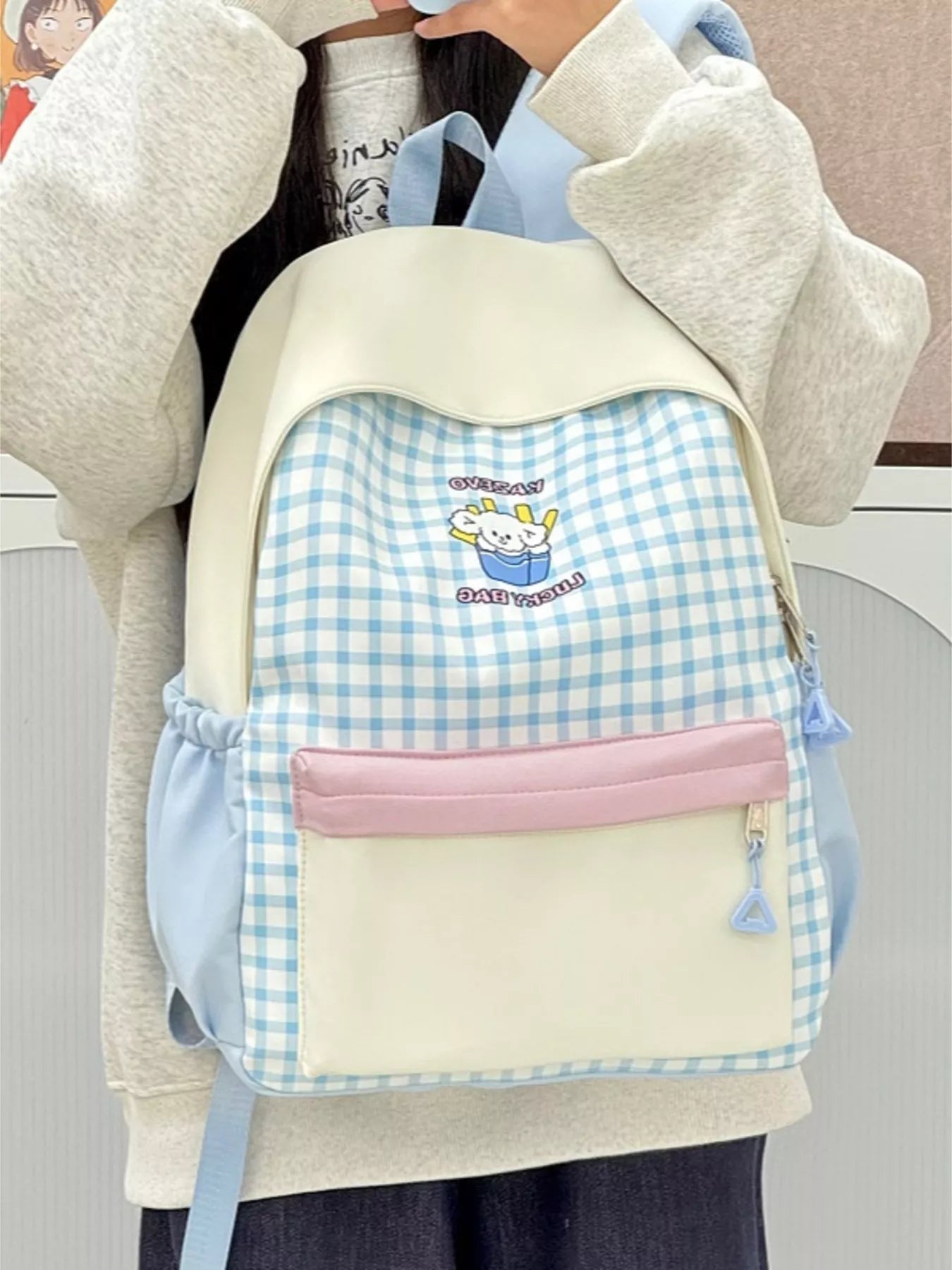 Blue gingham cartoon backpack with cream flap, pink front pouch, side cord zipper pull.