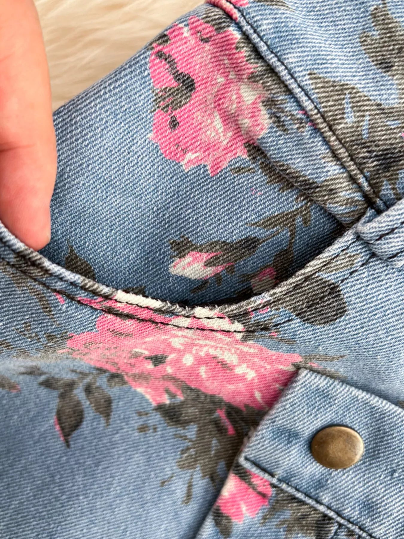 Blue denim skirt close-up with pink floral fabric, stitched waistband and gold button