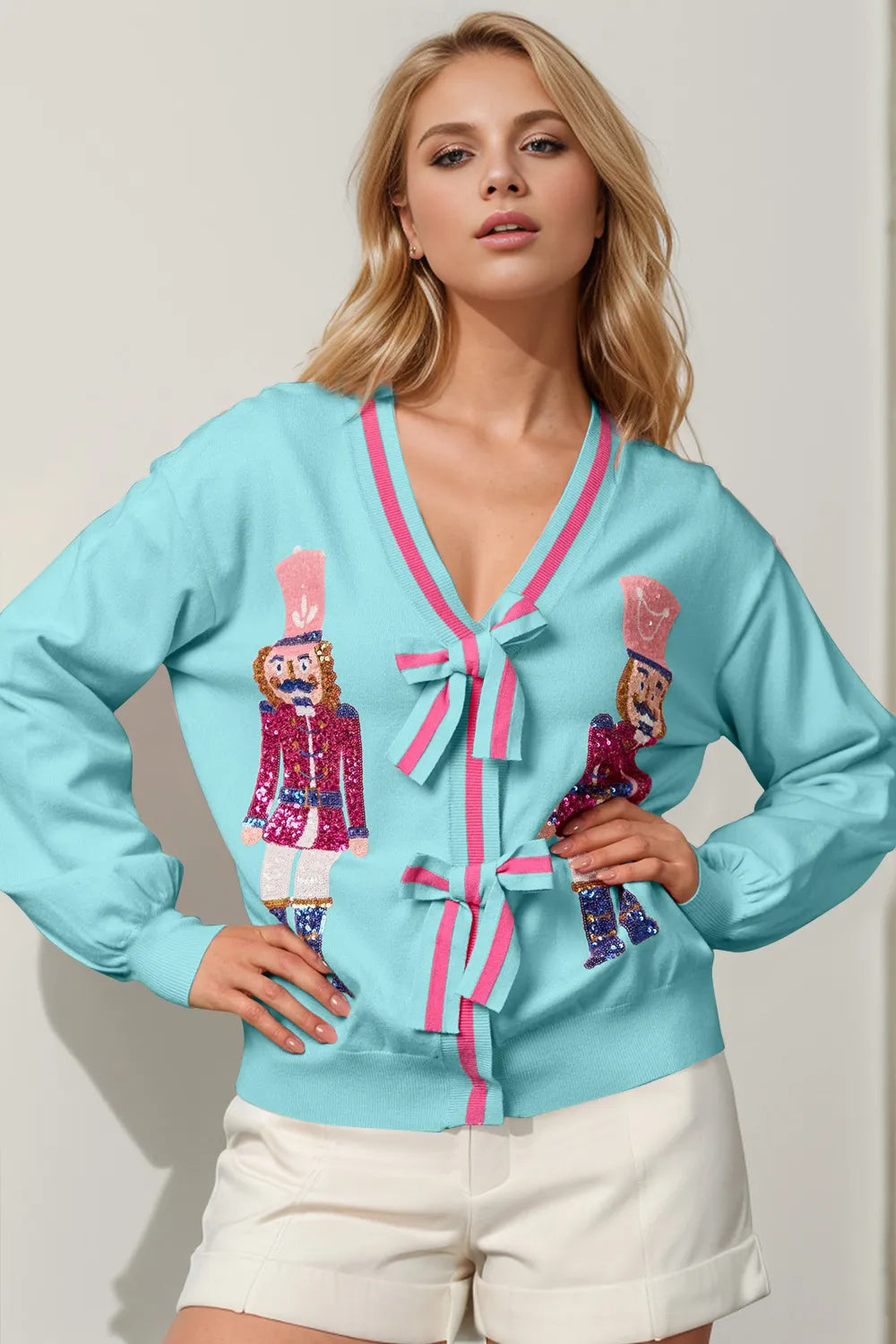 Woman wearing a light blue cardigan with pink trim and nutcracker designs on a plain background