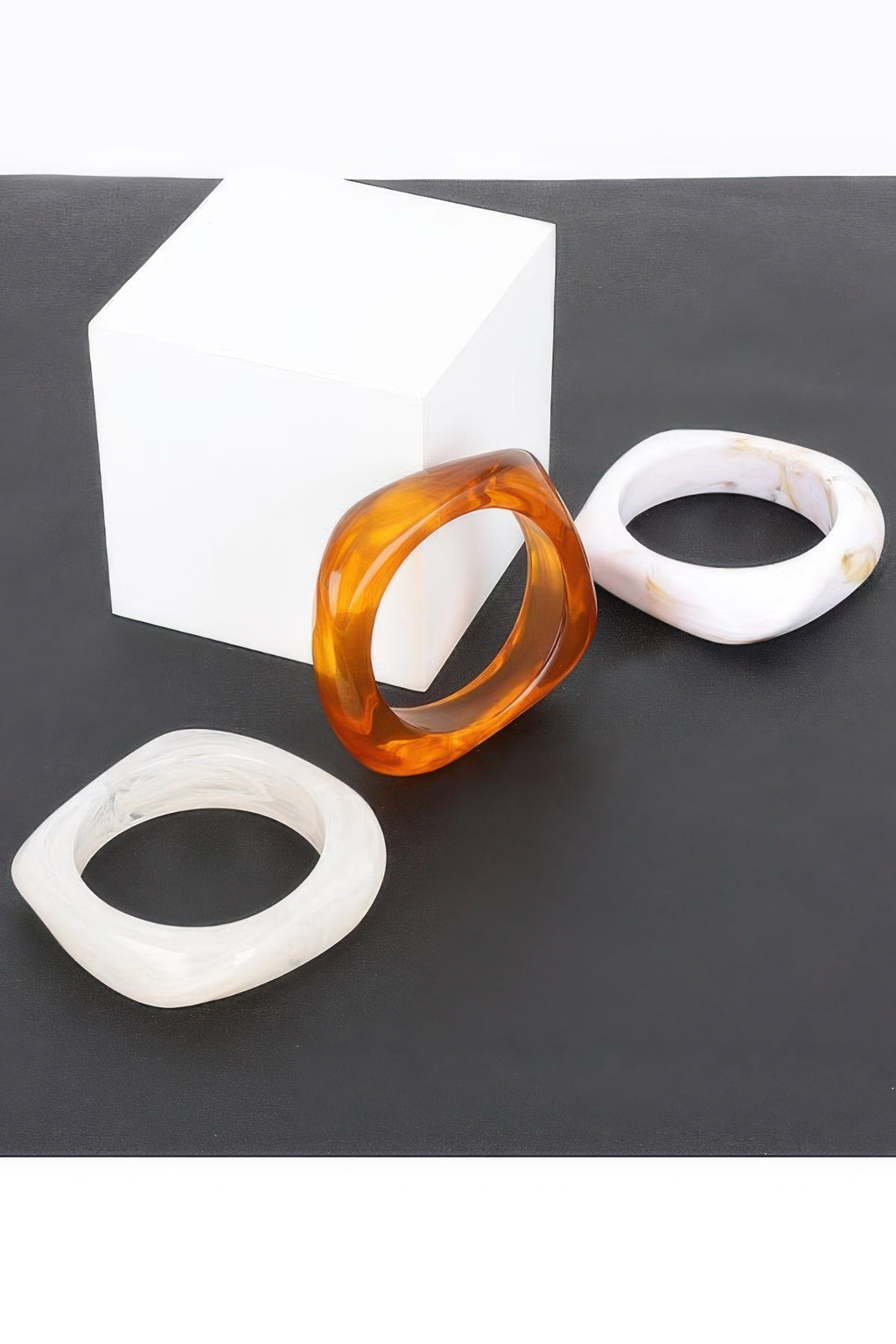 Three resin bangles: amber, translucent white, and white-gold marbling
