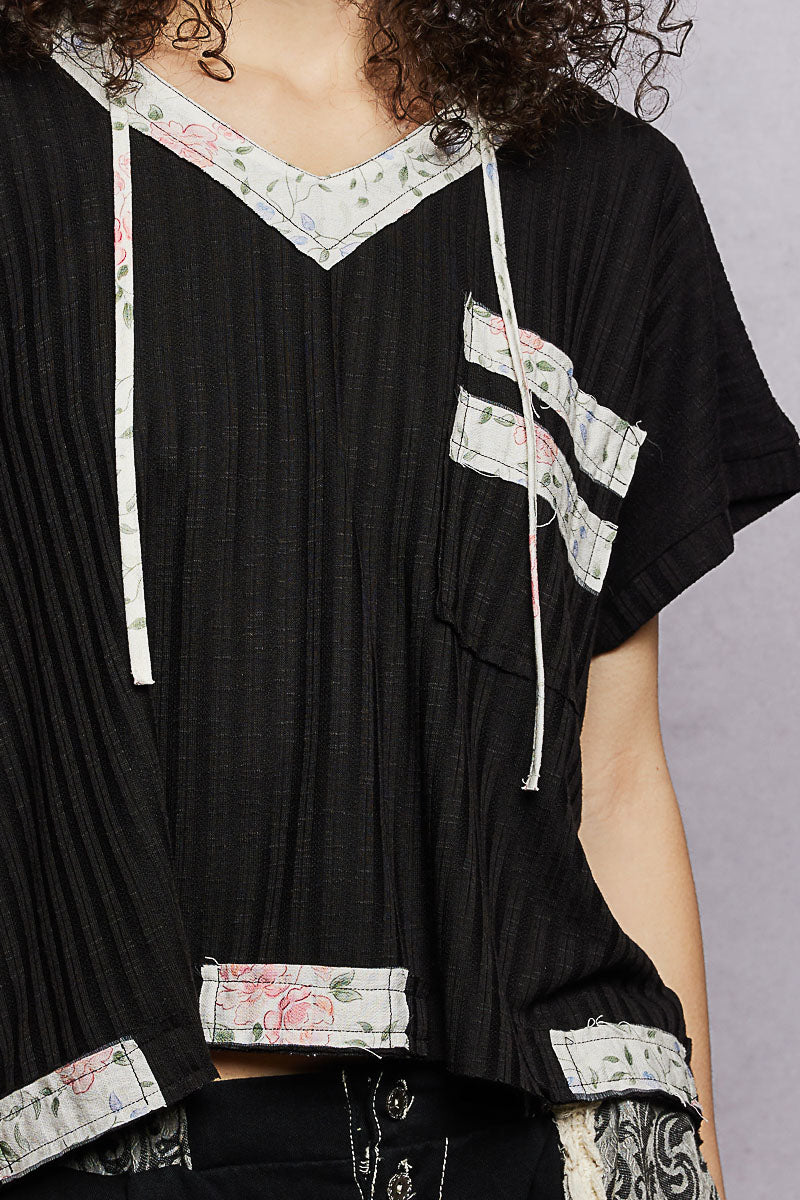 Detalle del top negro: capucha con cordones blancos y parche floral en el pecho