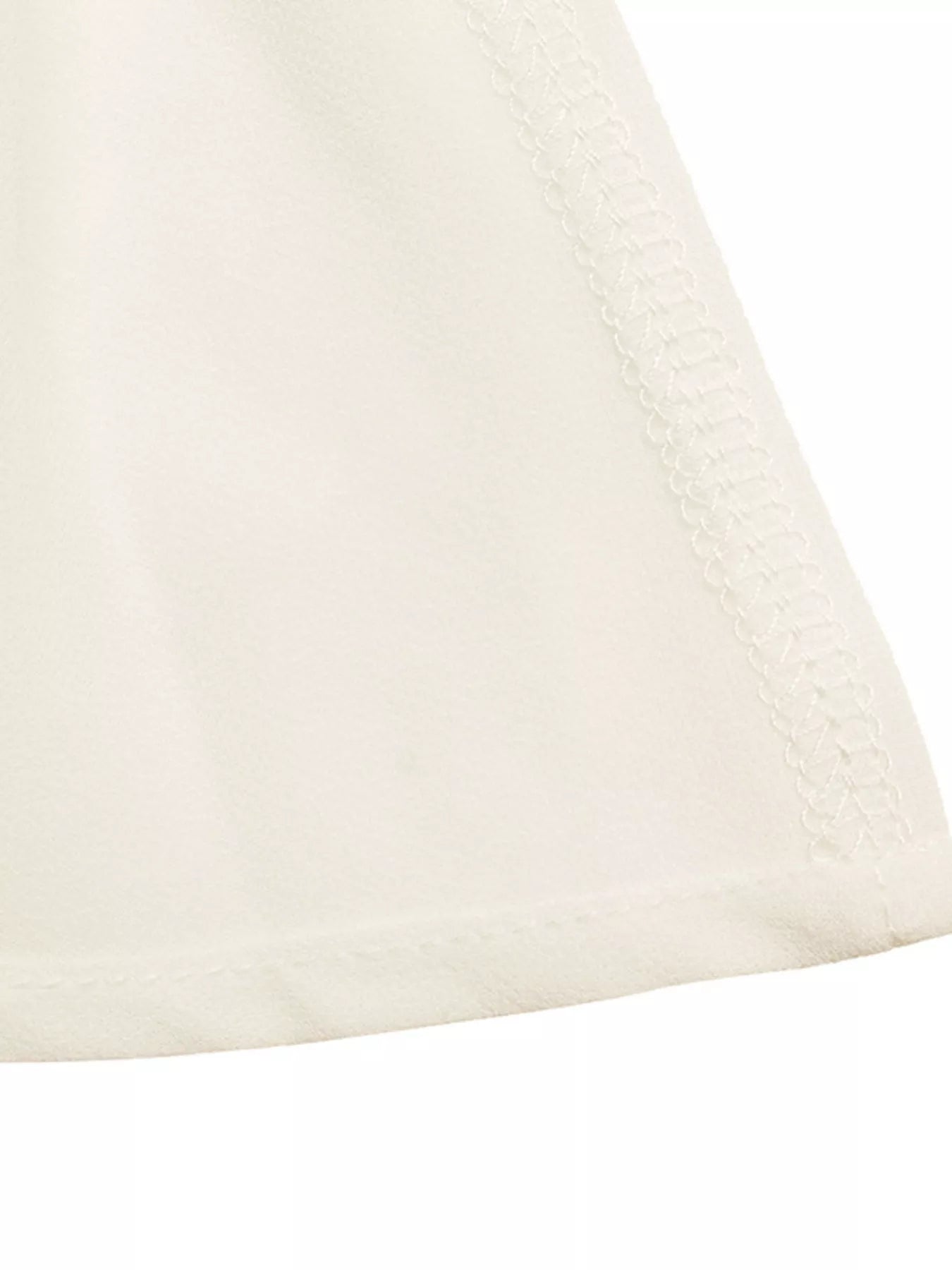 Close-up of white camisole hem with subtle texture and stitched trim edge