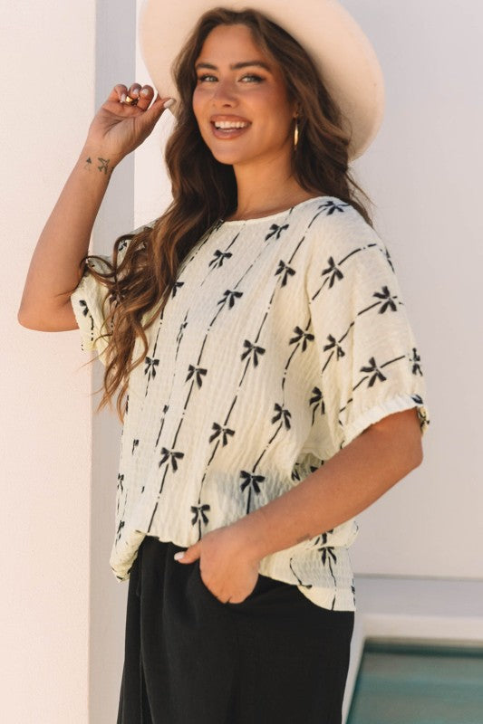 Cream bow-texture top with short puff sleeves and black bow print, relaxed fit