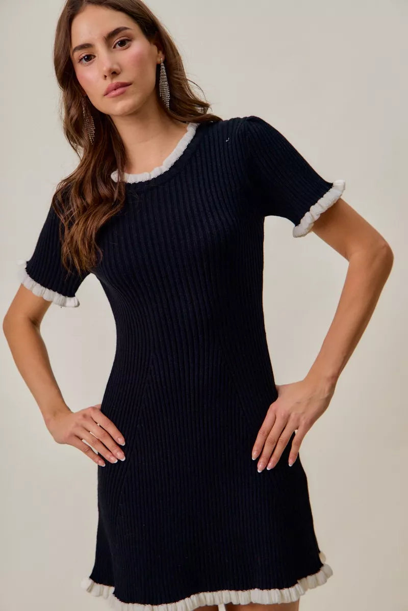 Black fitted knit mini dress, white ruffle-trim neckline and sleeves, ribbed texture