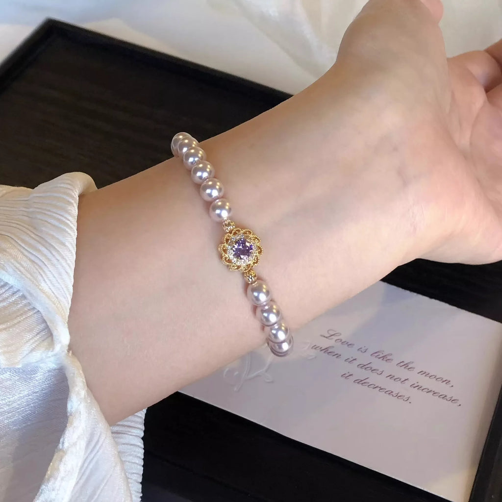 Pearl bracelet with gold flower centerpiece and purple-like center stone, shown on wrist