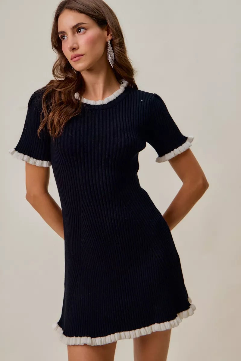 Black knit mini dress with white ruffle trim, short sleeves, fitted silhouette