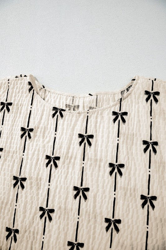 Close-up of cream bow-texture short puff sleeve top neckline with black bow pattern