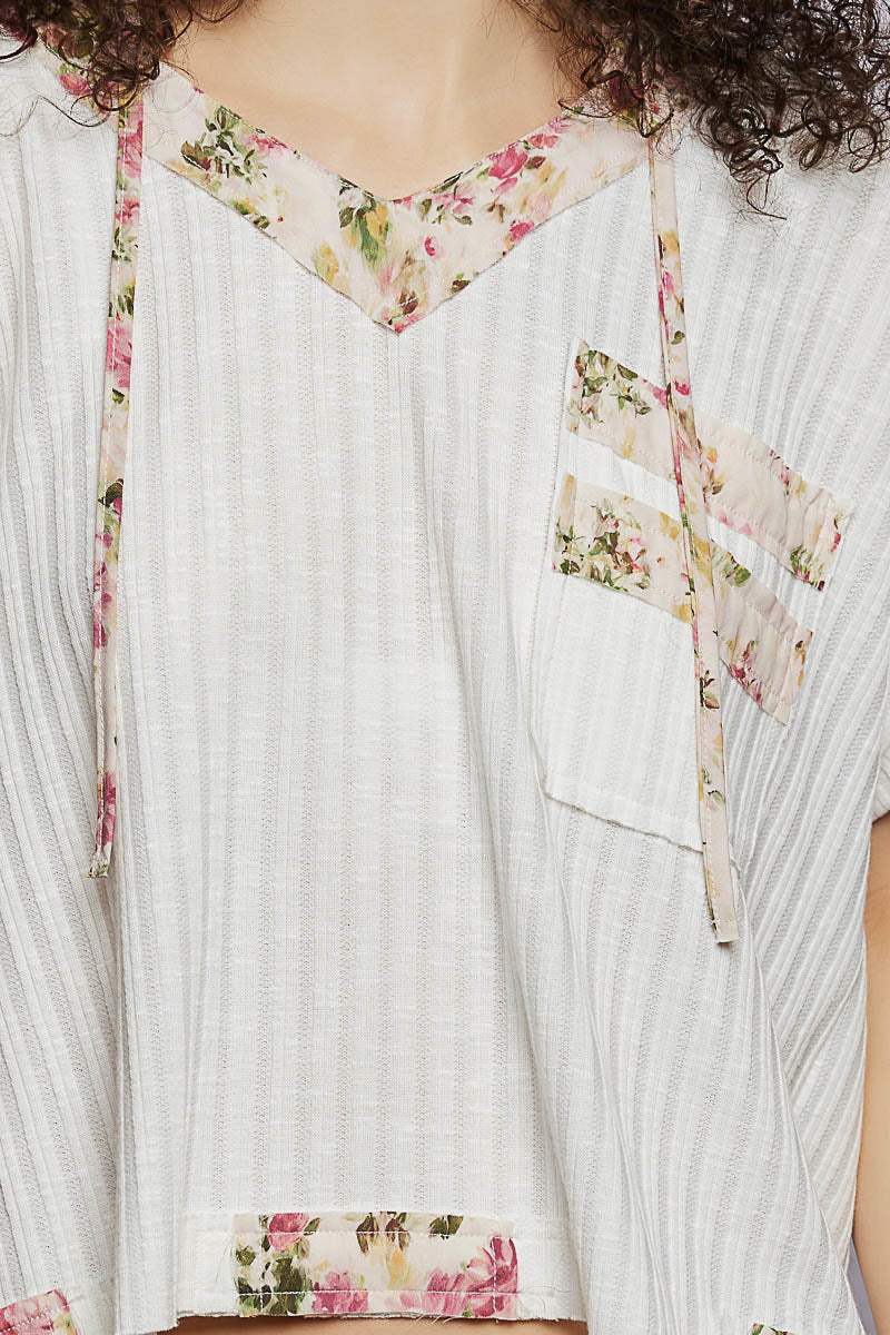 Close-up of off-white hooded top with floral-trim V-neck and chest pocket