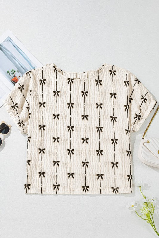 Cream short puff sleeve top laid flat, black bow-and-vertical stripe print, round neckline