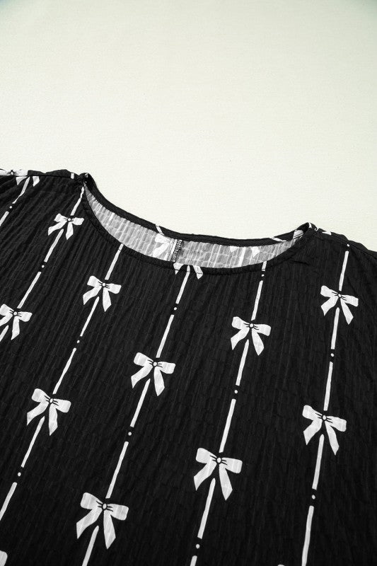 Black textured short puff-sleeve top close-up: bow print and elastic neckline