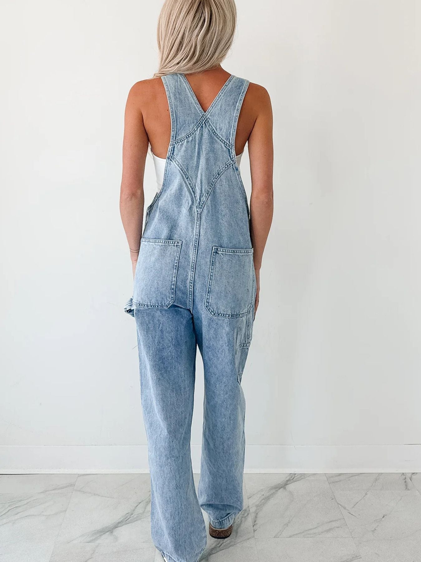 Back view of light blue denim relaxed overalls with crisscross straps