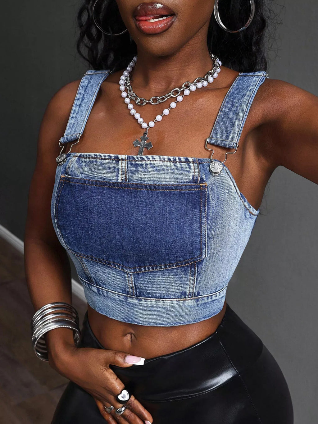 Close-up of blue cropped denim top: chest pocket, adjustable straps, center front seam
