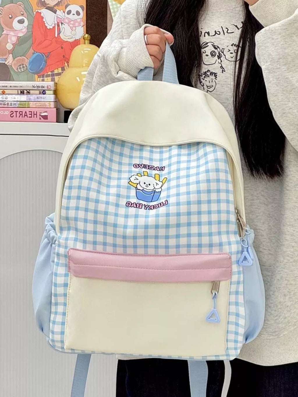 Front view of blue gingham cartoon backpack with pink front pouch and blue zipper pulls.
