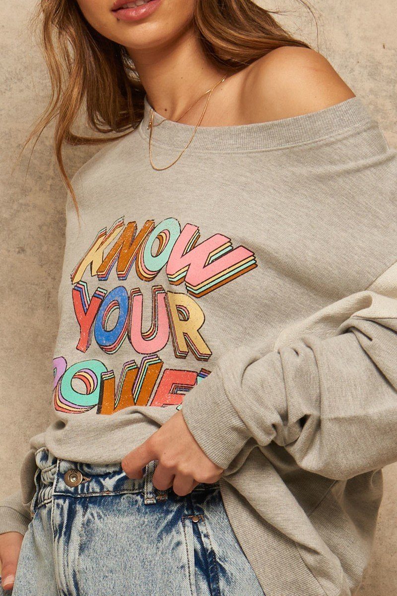 Light gray off-shoulder graphic sweatshirt with stacked rainbow “KNOW YOUR OWN POWER” text