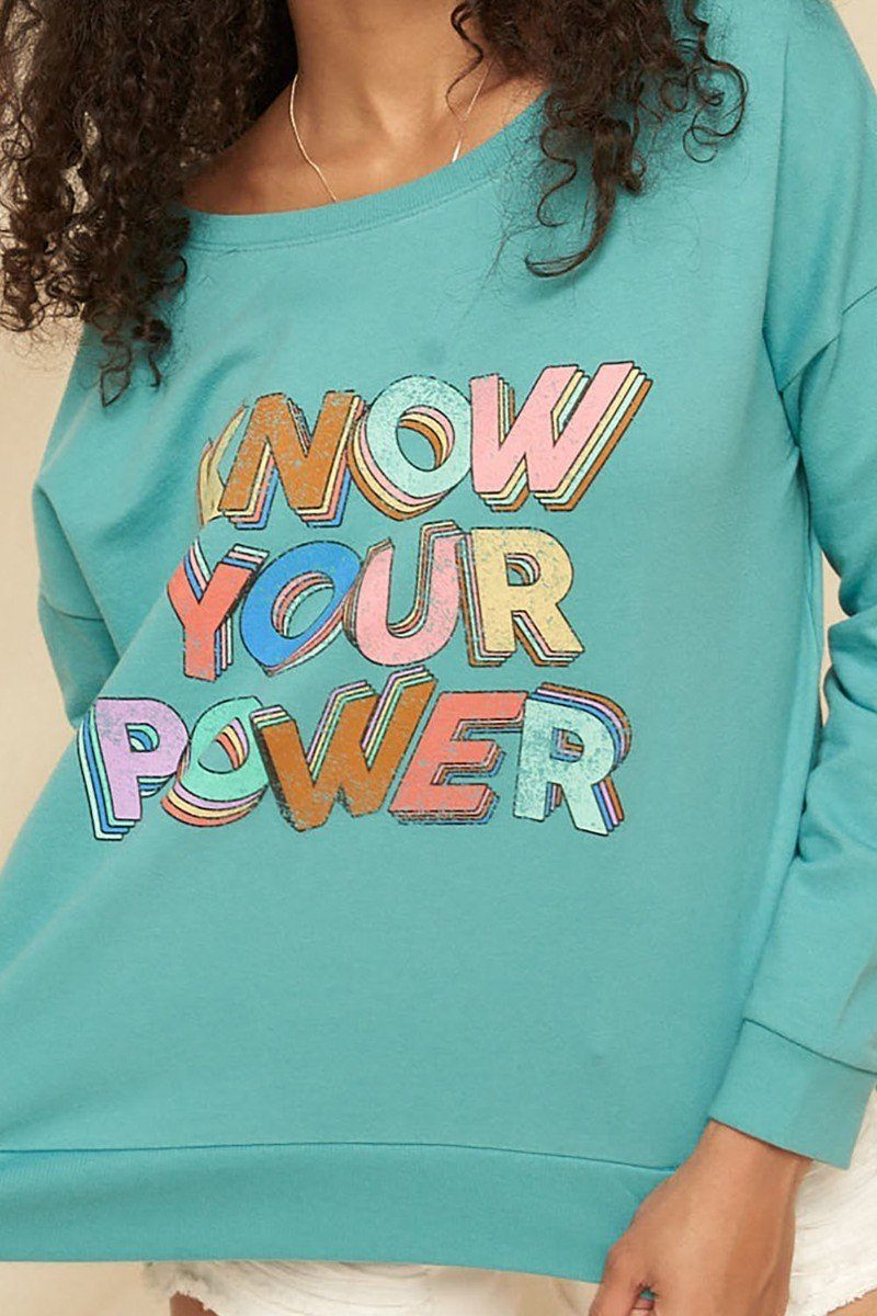 Close-up: turquoise sweatshirt with colorful “KNOW YOUR POWER” lettering graphic
