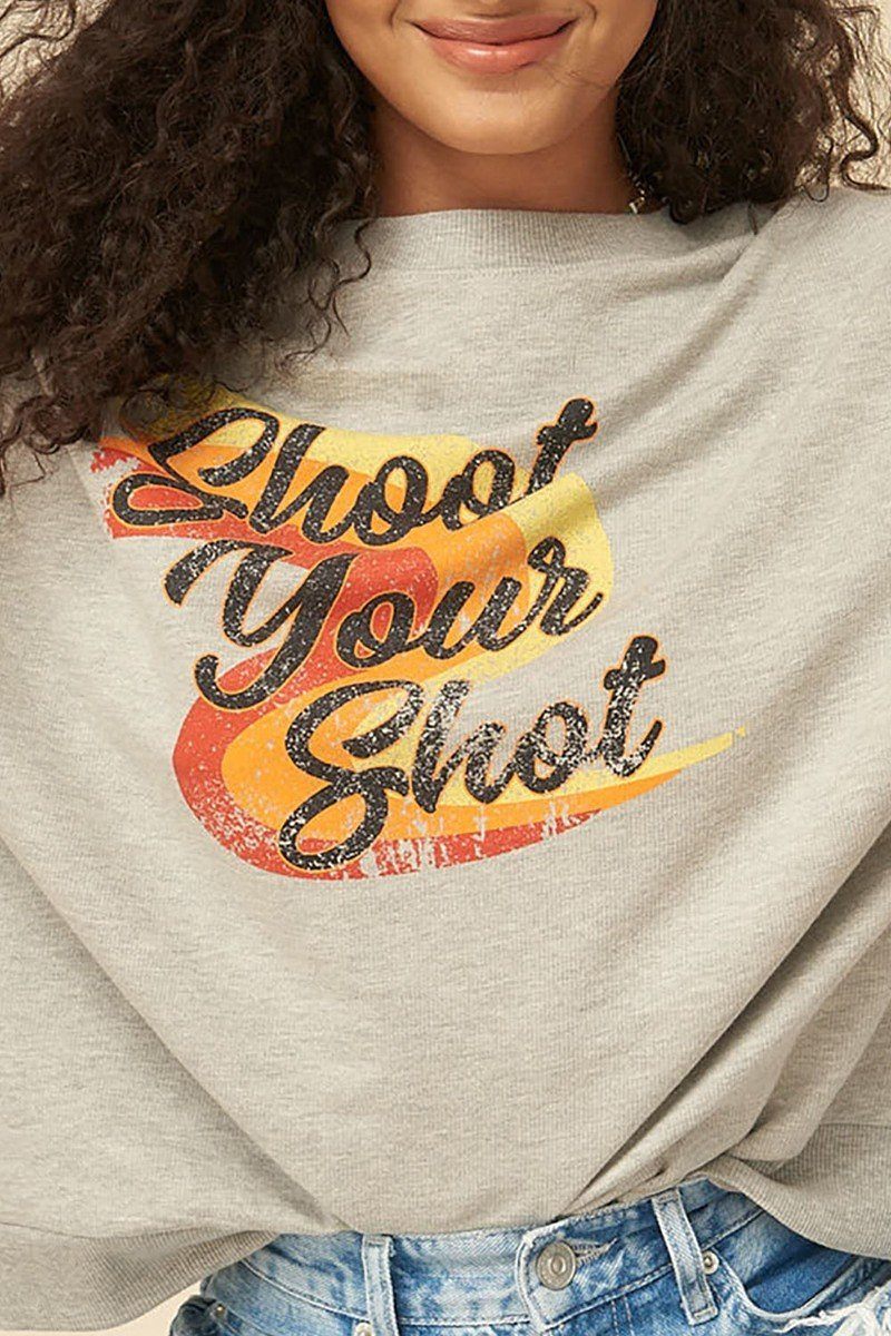 Gros plan sur le sweat gris clair, imprimé «Shoot Your Shot» en jaune, orange et rouge