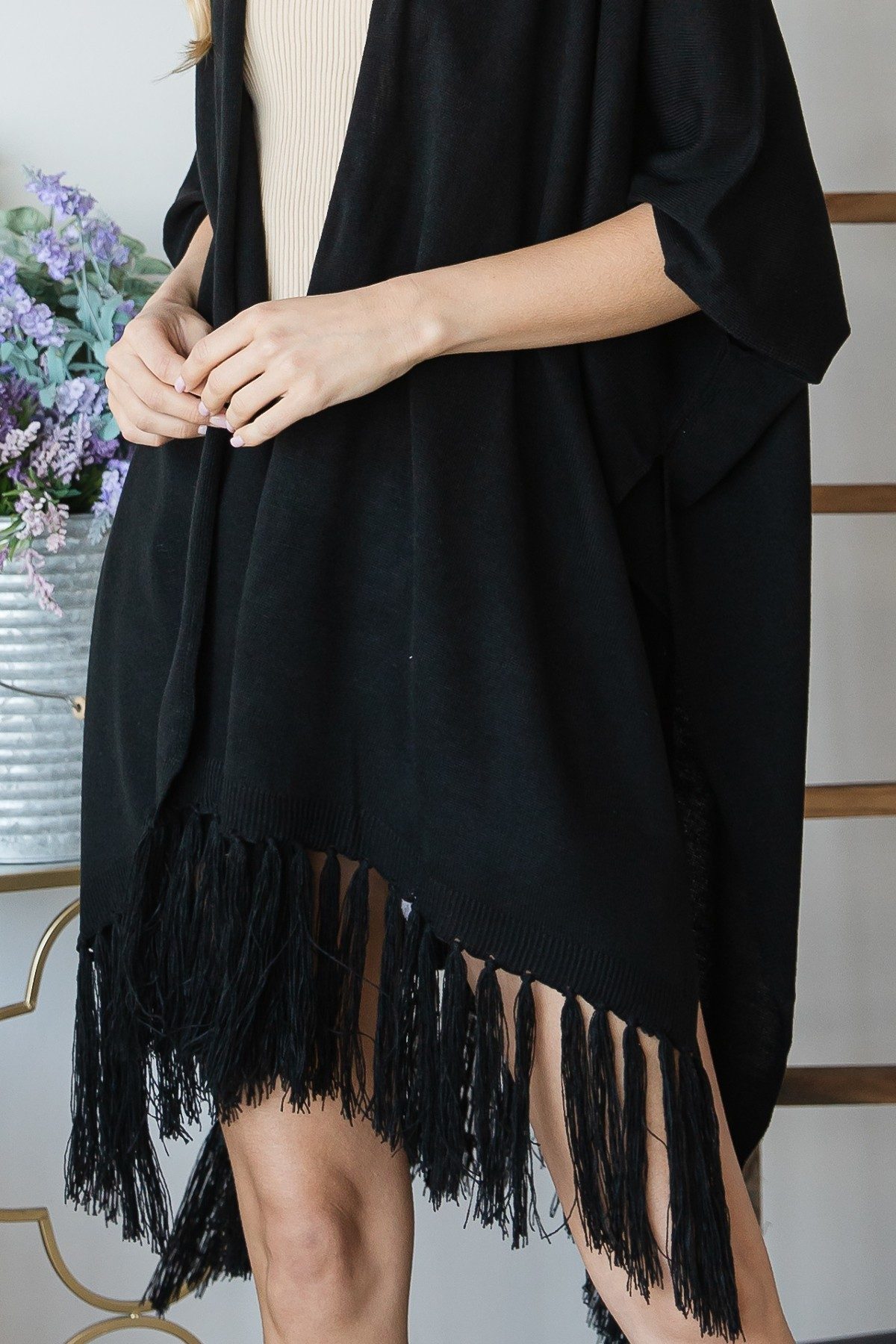 Close-up: black poncho cardigan with tassel fringe hem and string detail