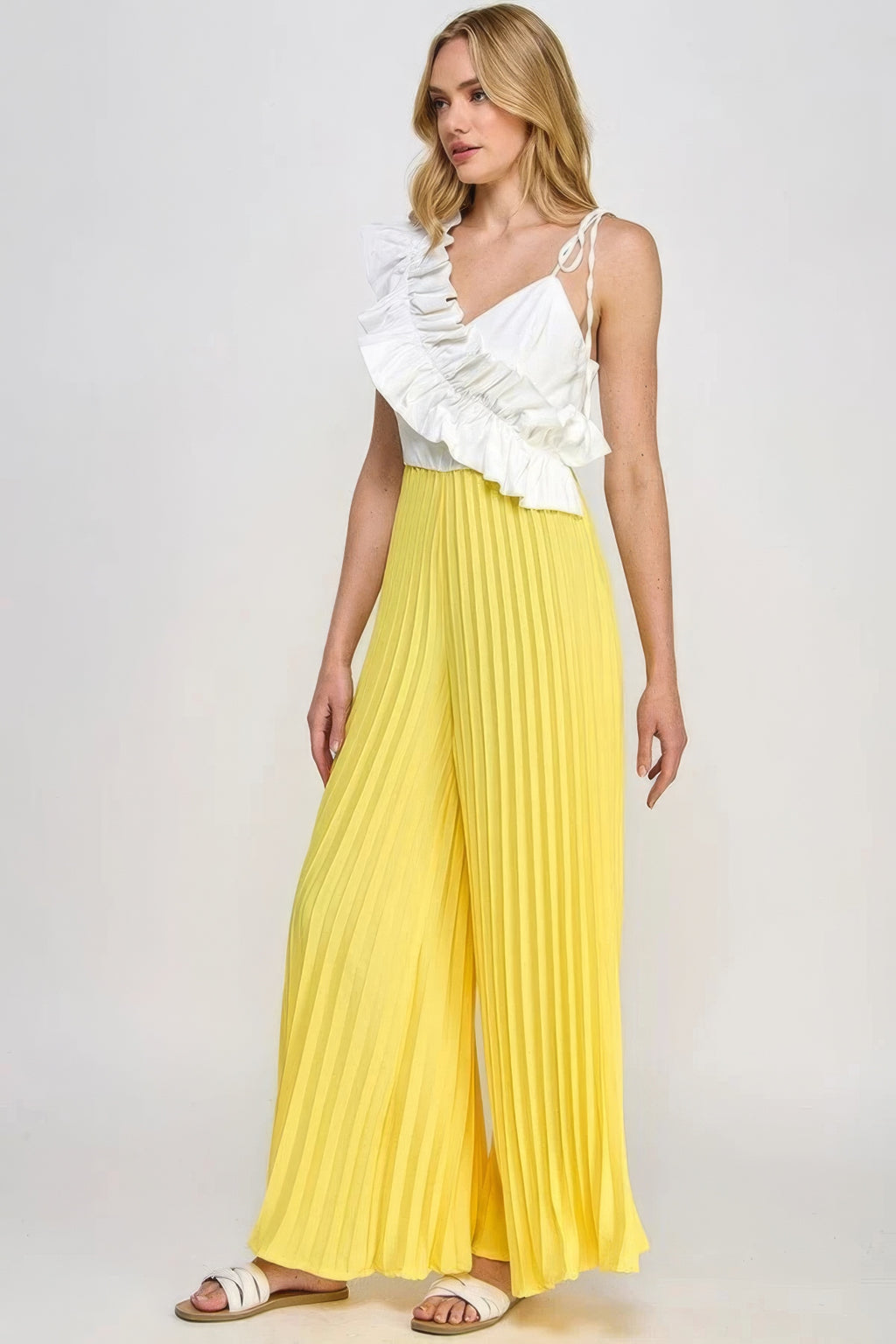Cami jumpsuit with tie spaghetti straps and white ruffle neckline; yellow pleated wide-leg