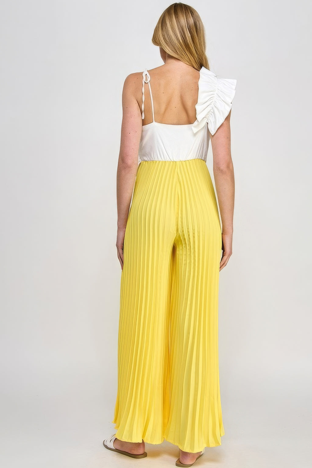 Back view: cami jumpsuit with open tie straps, white ruffle detail, yellow pleated wide legs