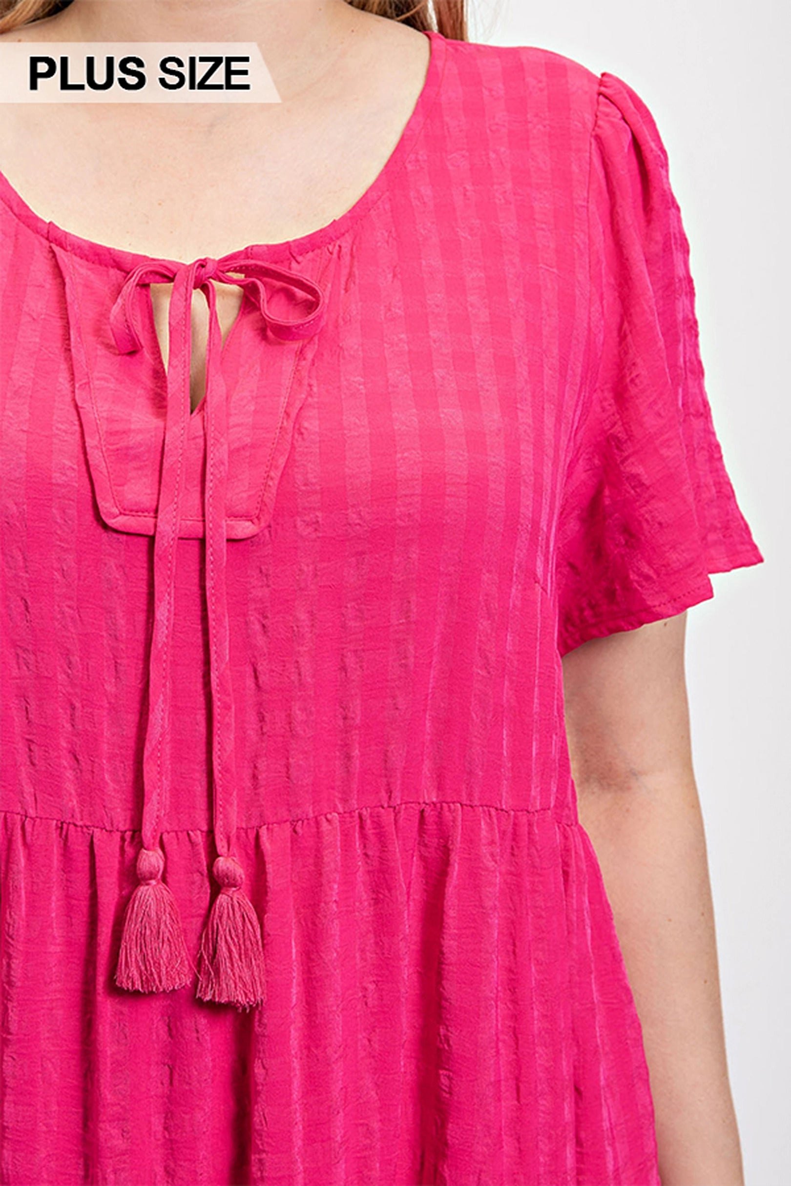 Close-up: fuchsia tassel-tie neckline on textured tiered dress