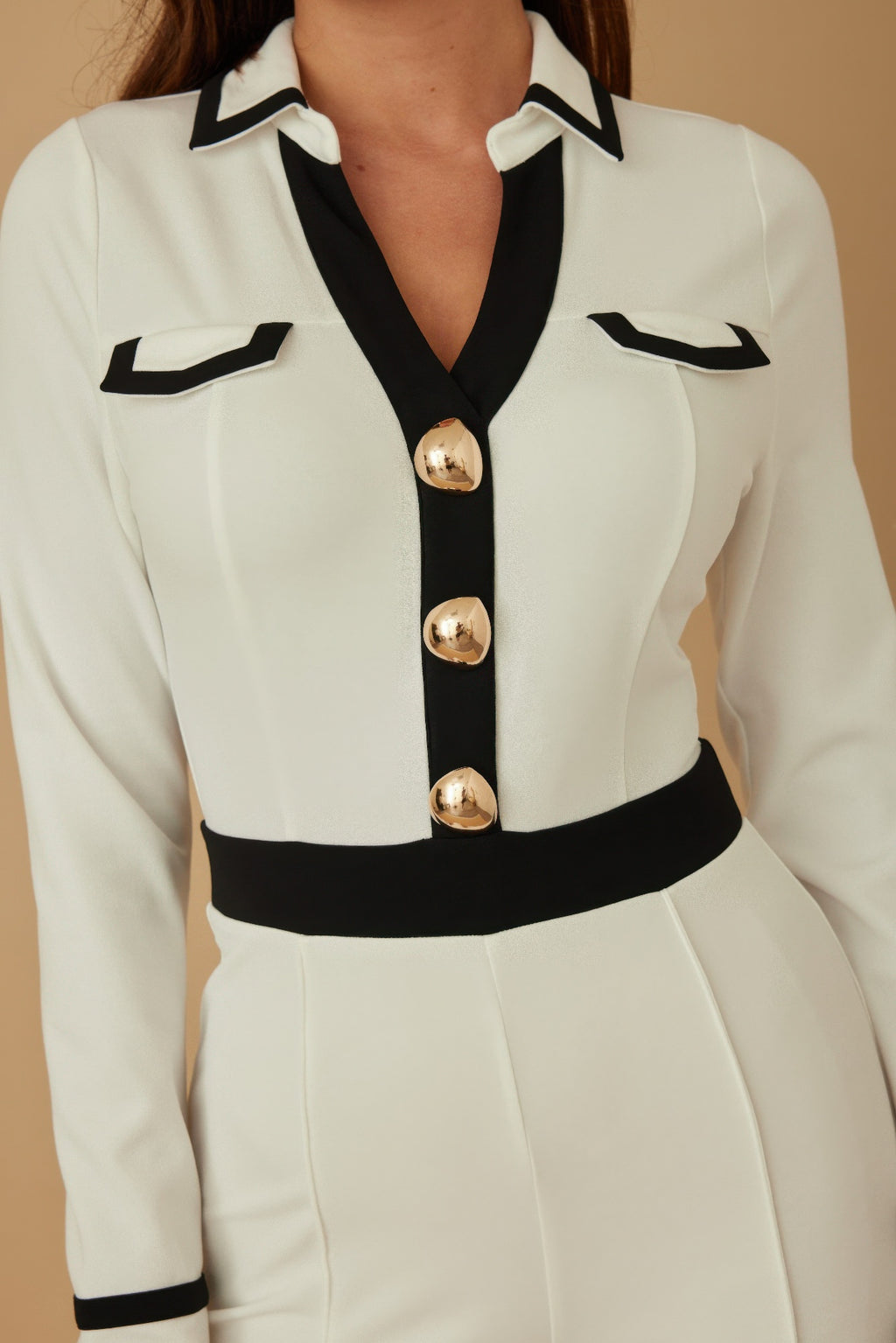 Close-up: cream jumpsuit bodice with black collar and three gold round buttons