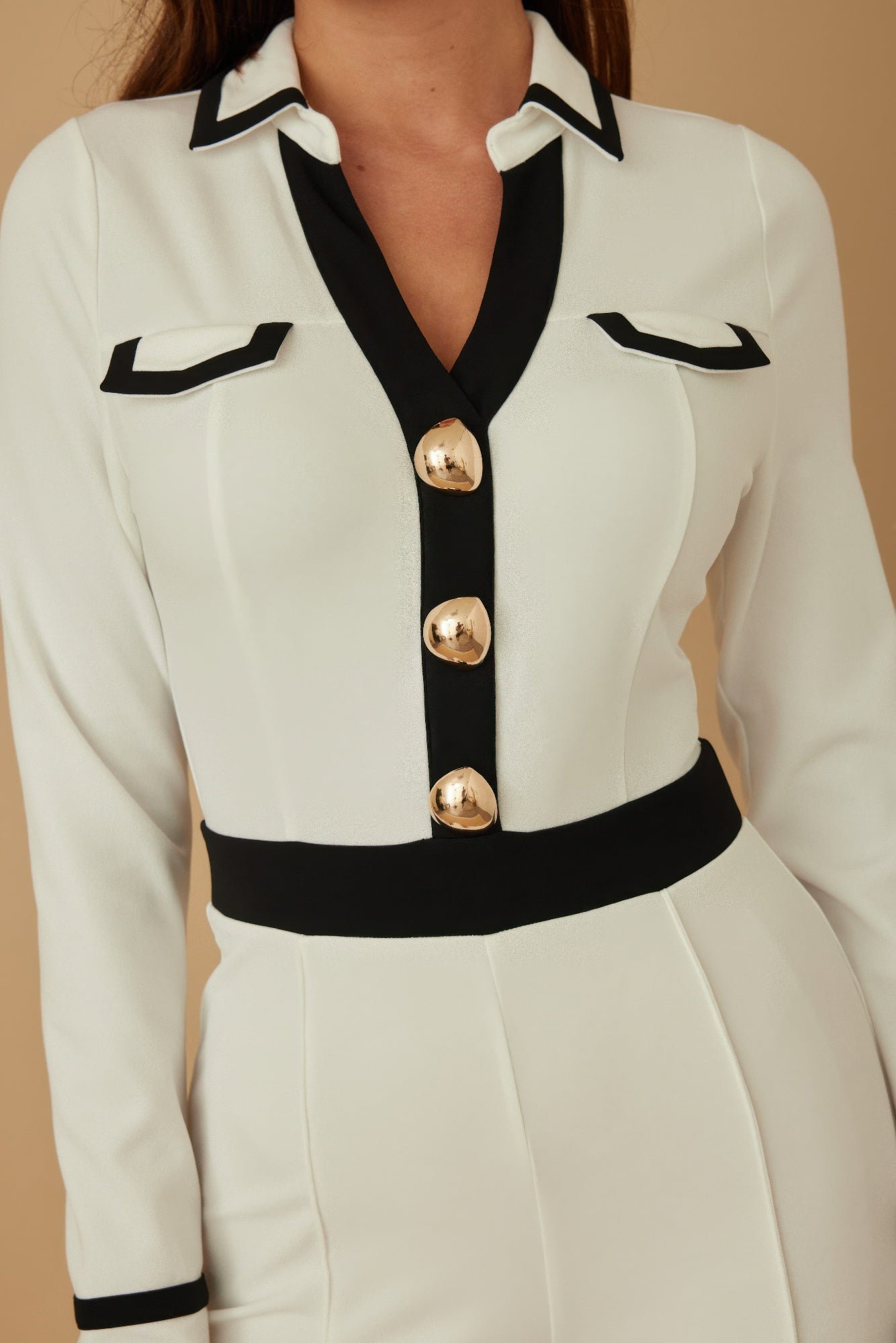 Close-up: cream jumpsuit bodice with black collar and three gold round buttons