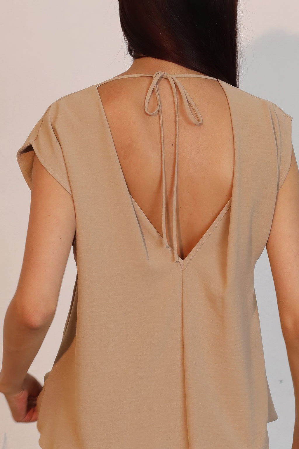 Close-up of tan open-back crepe top with V back neckline and tie strings.