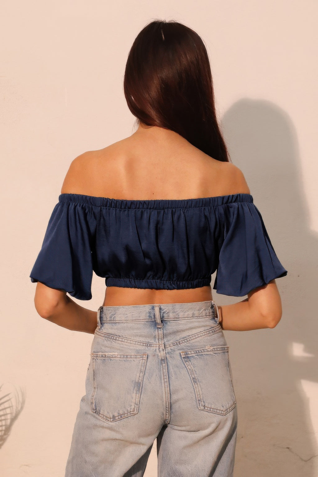 Back view: navy off-shoulder crop top with gathered waist and fluttery sleeve cuffs