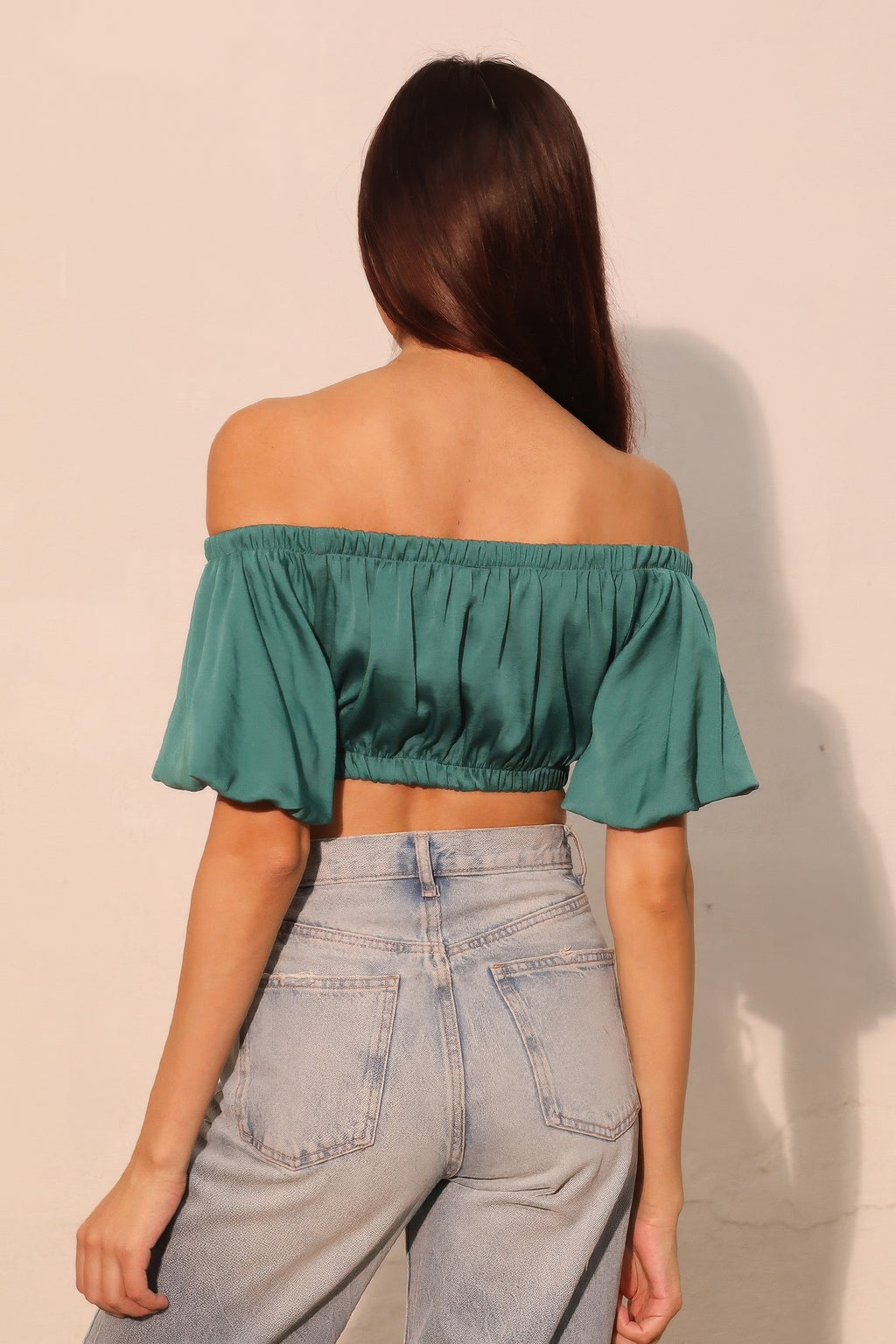 Back view: forest green off-shoulder crop top with elastic shirring and ruffle cuffs