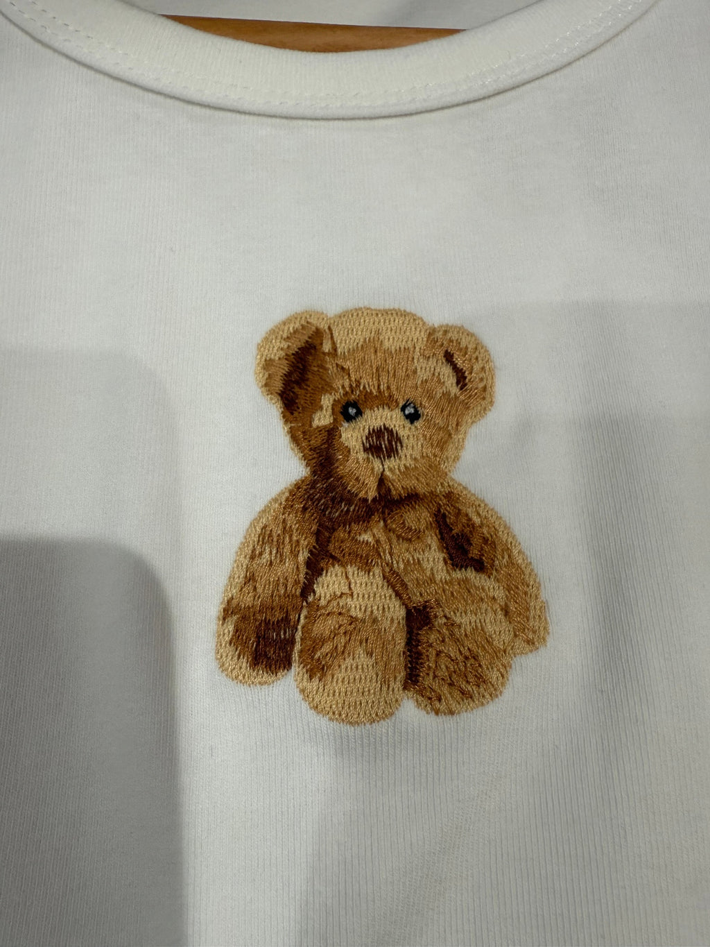 Close-up of white crop top with embroidered teddy bear applique
