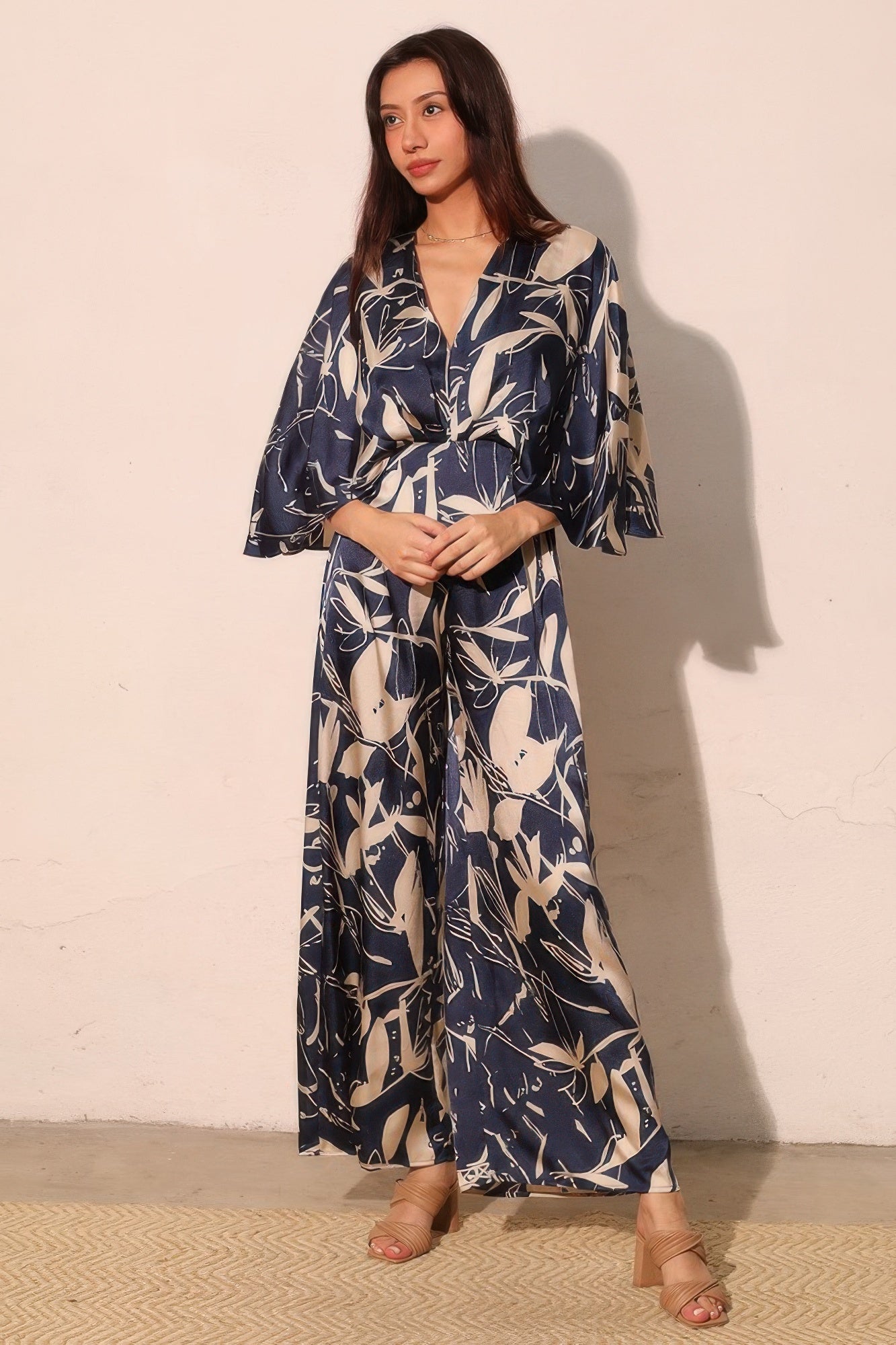 Navy satin jumpsuit with flutter cape sleeves, belted waist, and wide legs