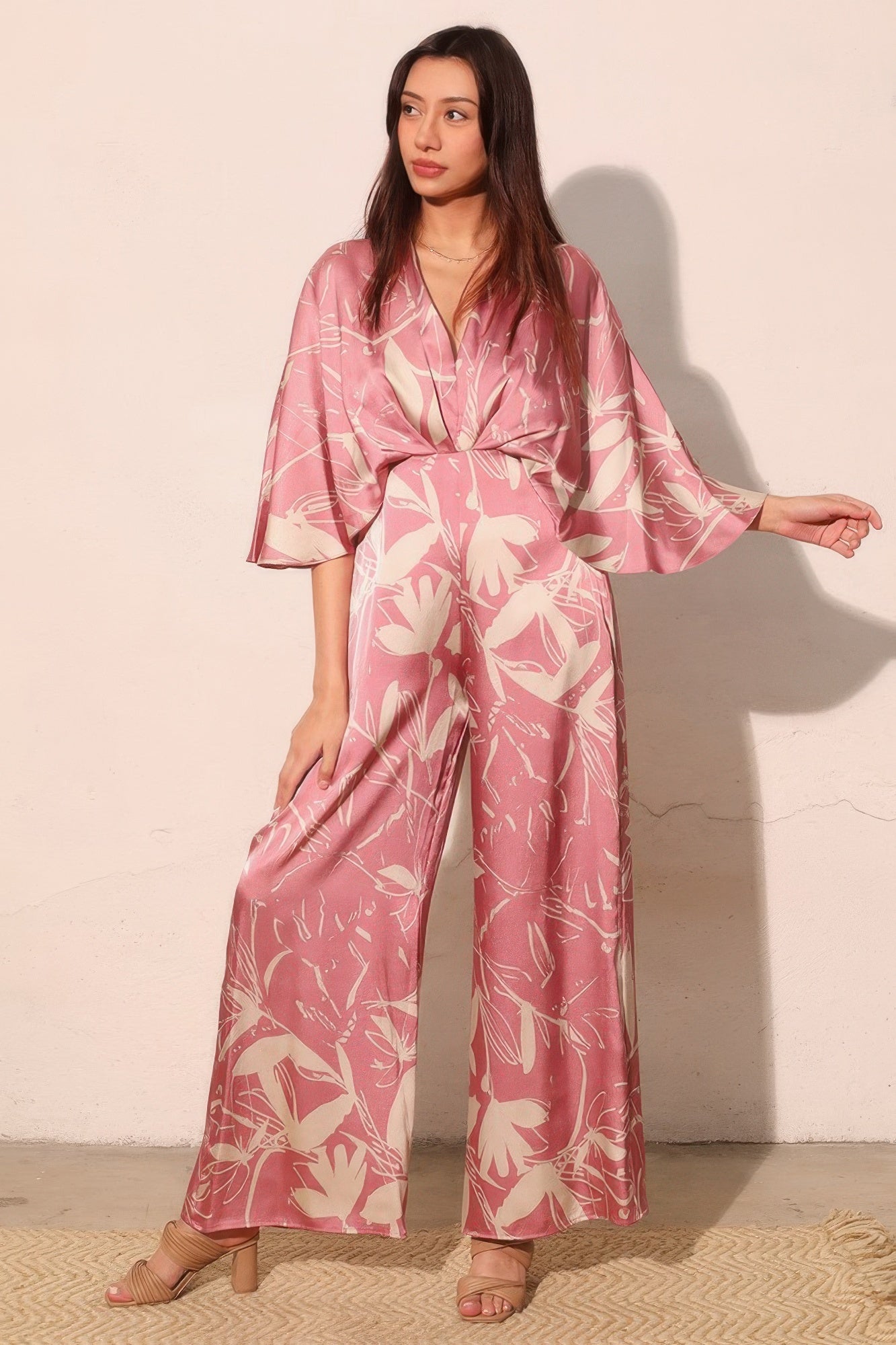 Pink satin jumpsuit with floral print, cape sleeves, V-neck, tie waist, wide-leg pants
