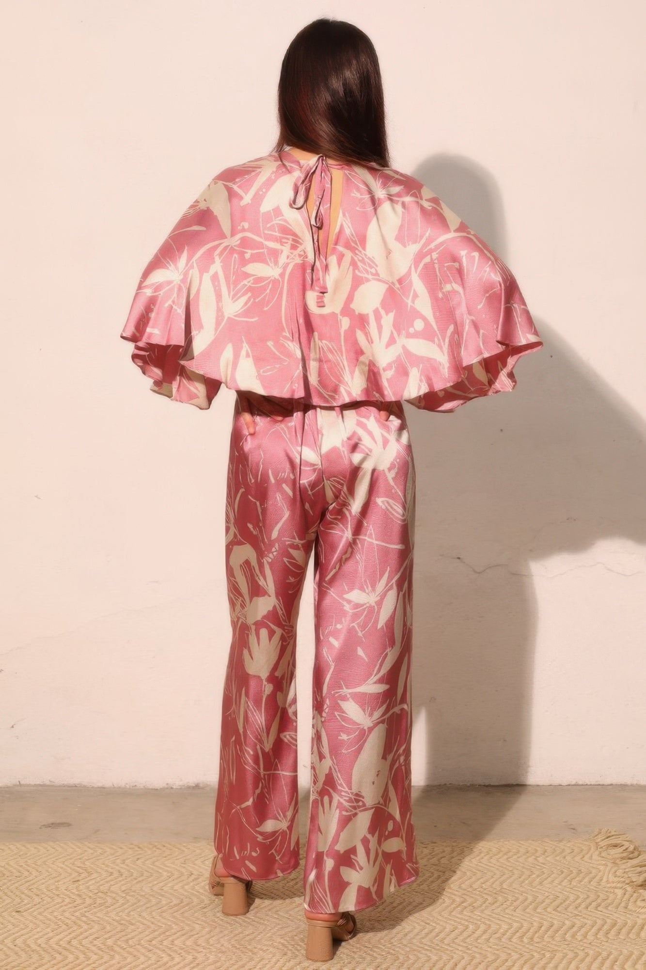 Pink satin jumpsuit back view with keyhole tie and flowing cape drape, floral print