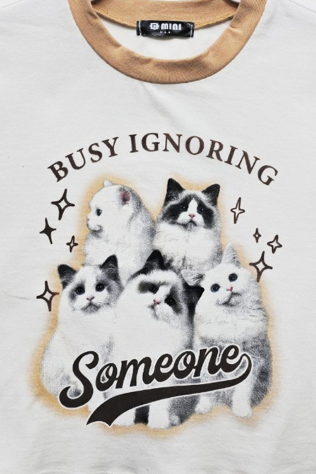 Close-up of white T-shirt neckline and 'Busy Ignoring Someone' cat print