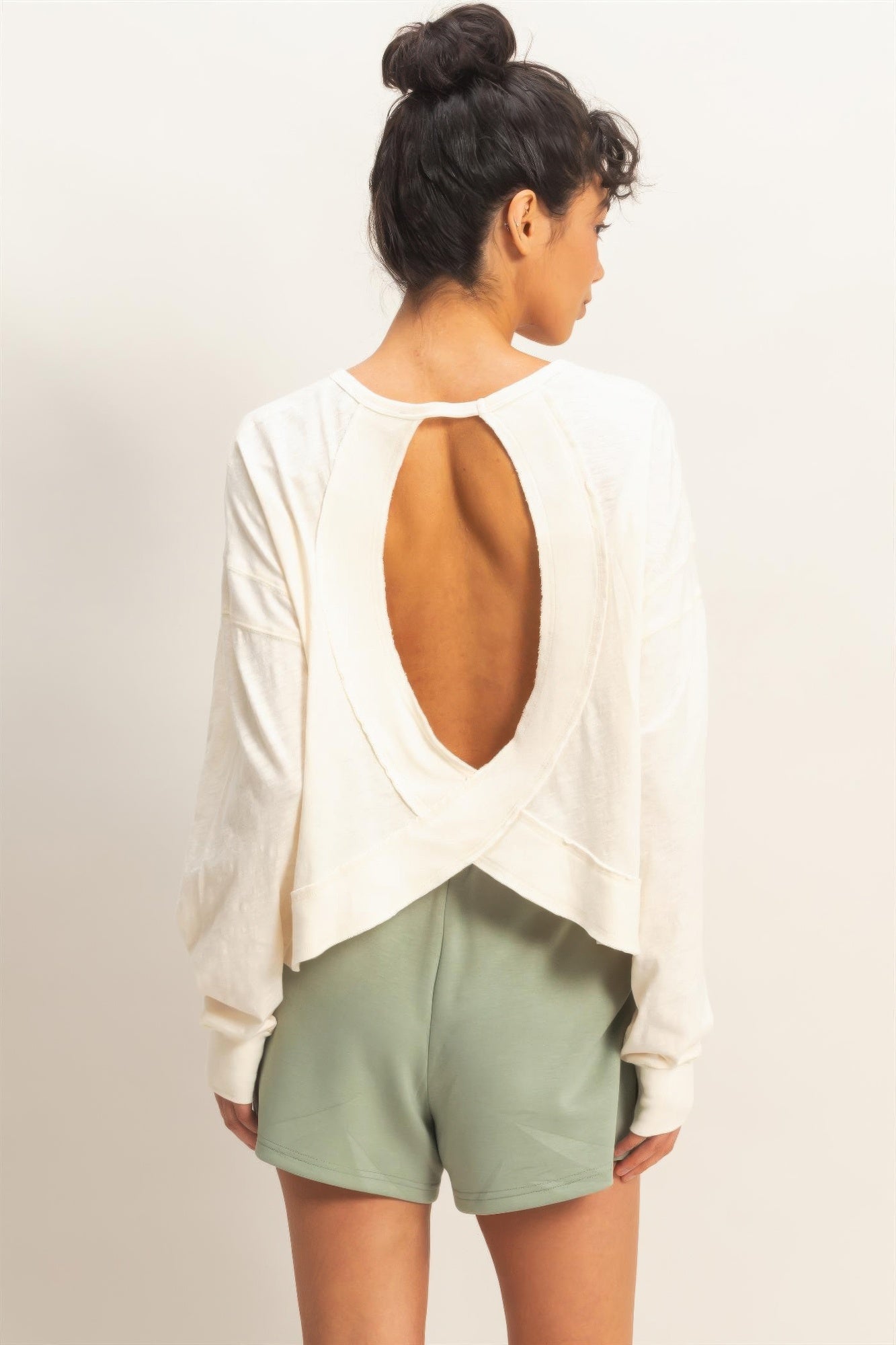 Back view: white long-sleeve top with deep oval open back and cross-over strap design