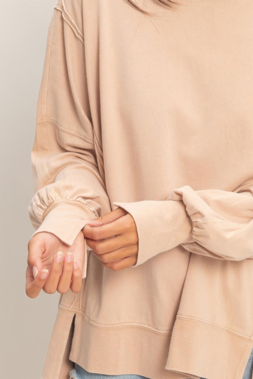 Close-up of taupe oversized long sleeve top cuff with seam stitching and relaxed hem