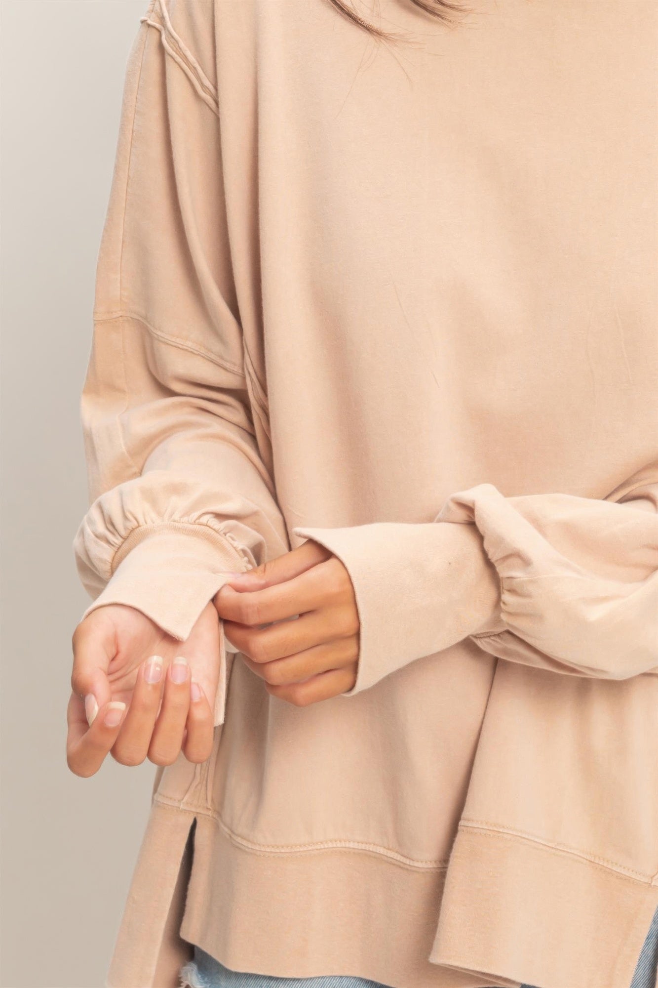 Close-up of taupe oversized long sleeve top cuff with seam stitching and relaxed hem