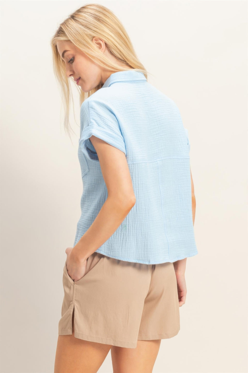 Back view of rolled-sleeve button-up top in light blue with curved hem